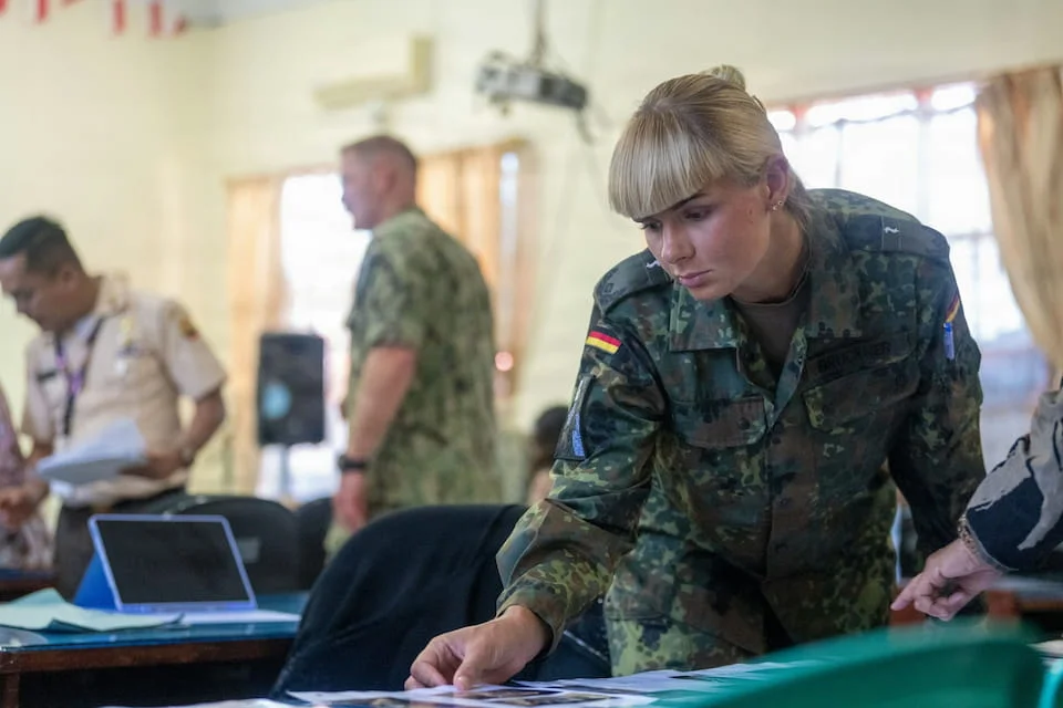 A woman in a military uniform is looking at documents at a table.