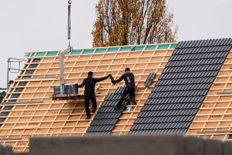 Workers laying roof tiles on a new building.