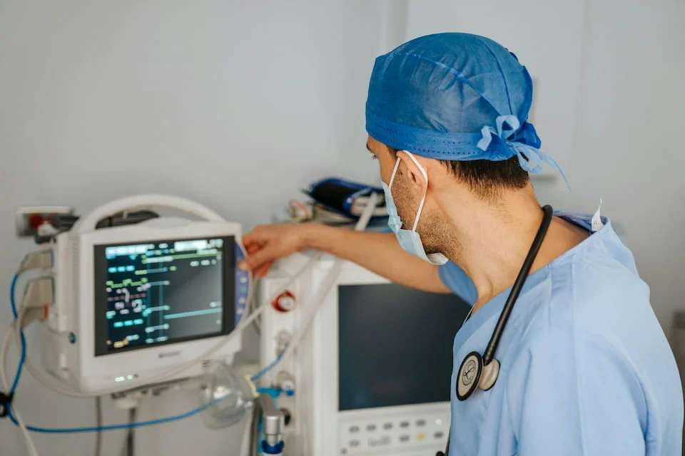 A man wearing scrubs and a stethoscope, looking at a monitor.